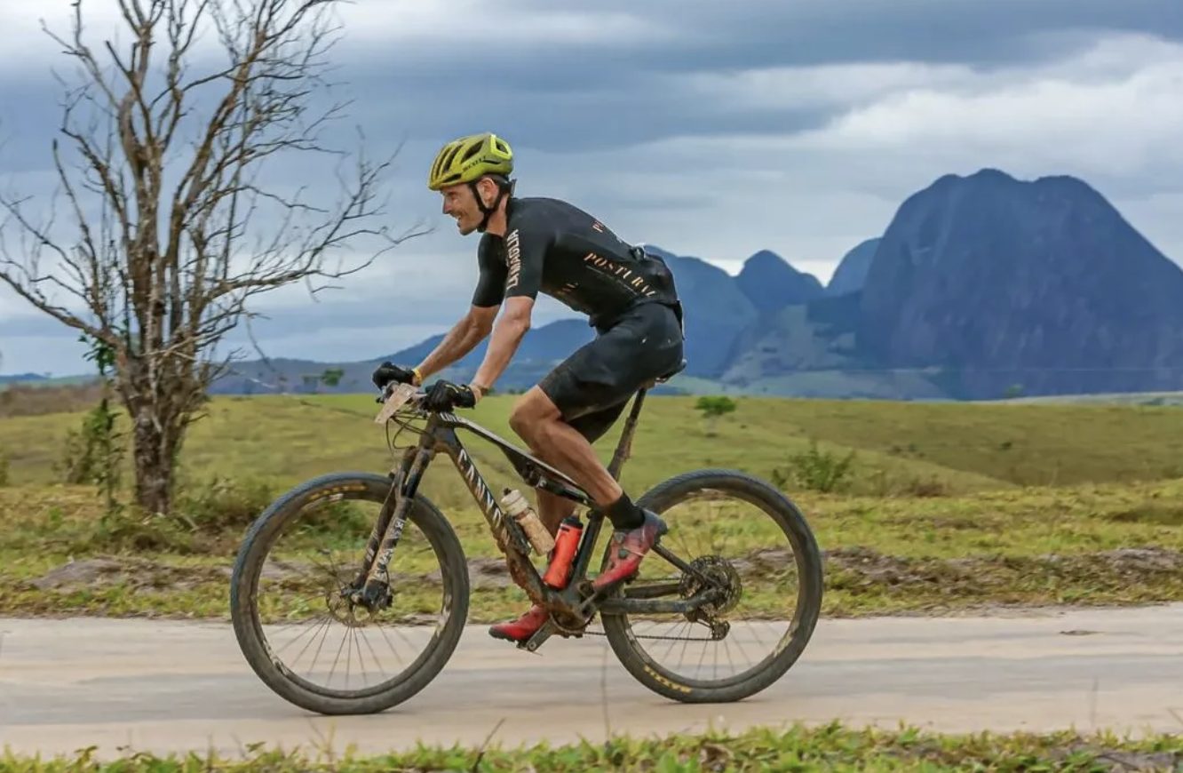 Lukas Kaufmann pedalando numa estrada de terra, com montanhas de pedra ao fundo
