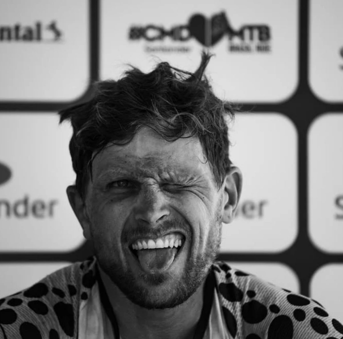 Retrato em preto e branco de Lukas Kaufmann piscando e mostrando a língua, depois de uma prova